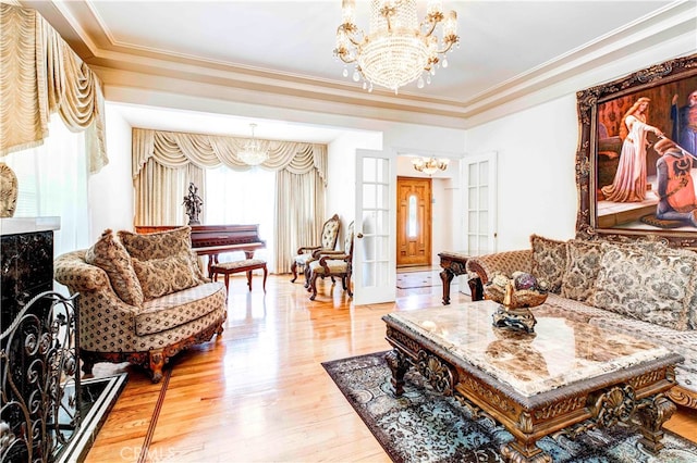 living room with ornamental molding, a tray ceiling, a chandelier, and light hardwood / wood-style floors