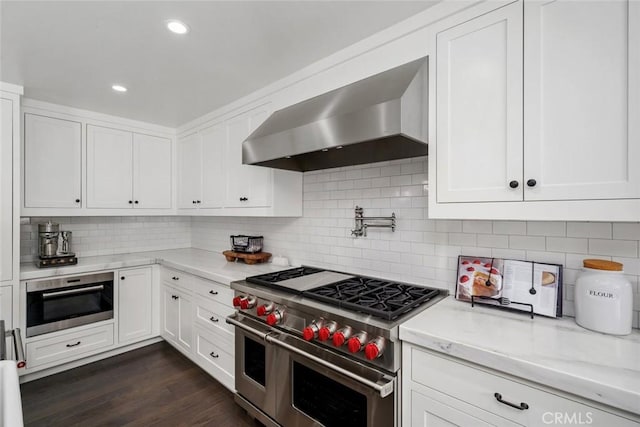 kitchen with wall chimney exhaust hood, stainless steel appliances, light stone counters, dark hardwood / wood-style flooring, and white cabinets