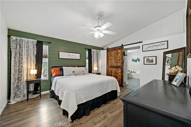 bedroom featuring ceiling fan, lofted ceiling, a barn door, ensuite bath, and hardwood / wood-style floors