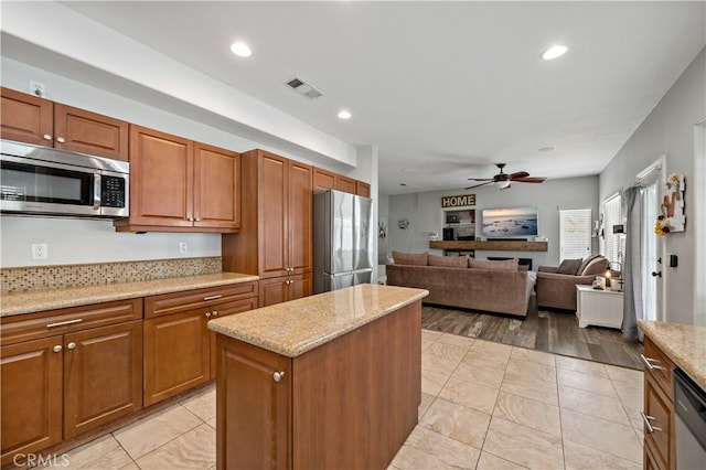 kitchen featuring light wood-type flooring, light stone counters, a kitchen island, stainless steel appliances, and ceiling fan