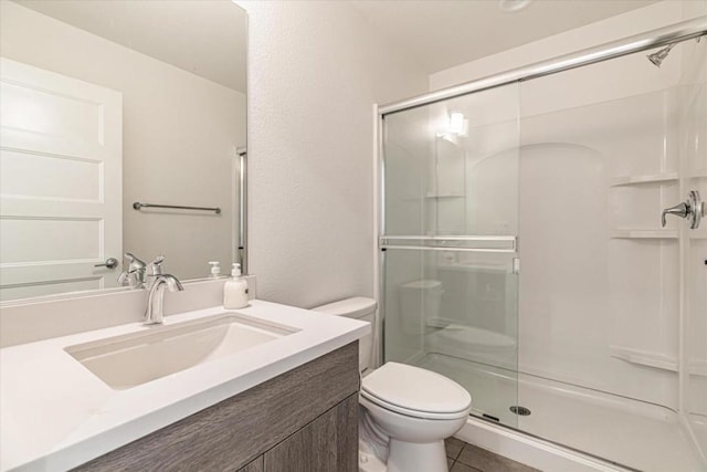 bathroom with a shower with door, vanity, tile patterned flooring, and toilet