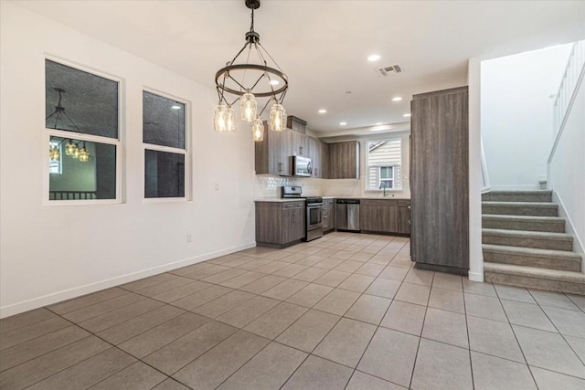 kitchen featuring pendant lighting, light tile patterned floors, sink, backsplash, and stainless steel appliances