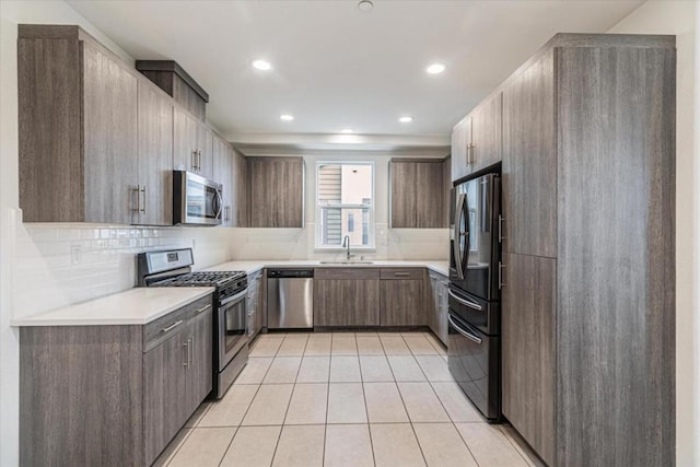 kitchen featuring appliances with stainless steel finishes, sink, light tile patterned floors, and decorative backsplash