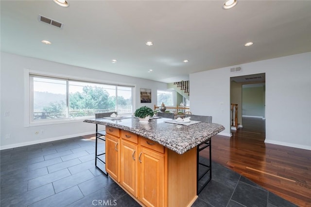 kitchen with a breakfast bar area, light stone countertops, dark hardwood / wood-style flooring, and a kitchen island