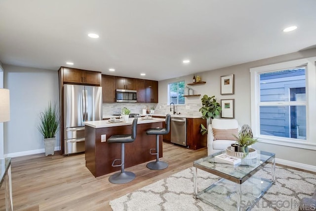 kitchen featuring a kitchen island, light wood-type flooring, backsplash, and appliances with stainless steel finishes