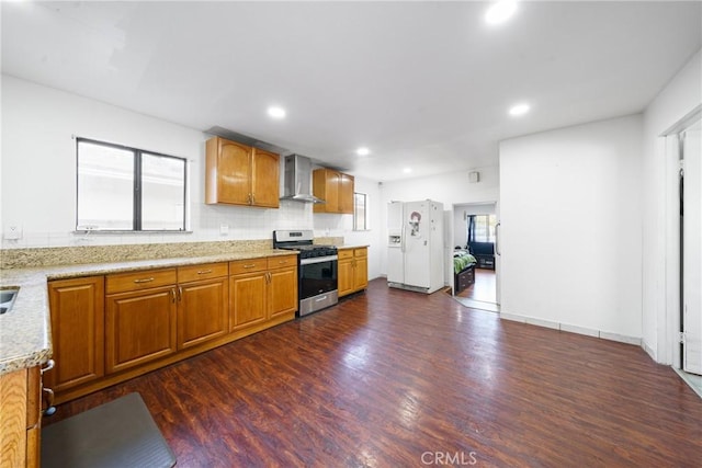 kitchen with dark wood-type flooring, wall chimney range hood, white fridge with ice dispenser, light stone countertops, and stainless steel range