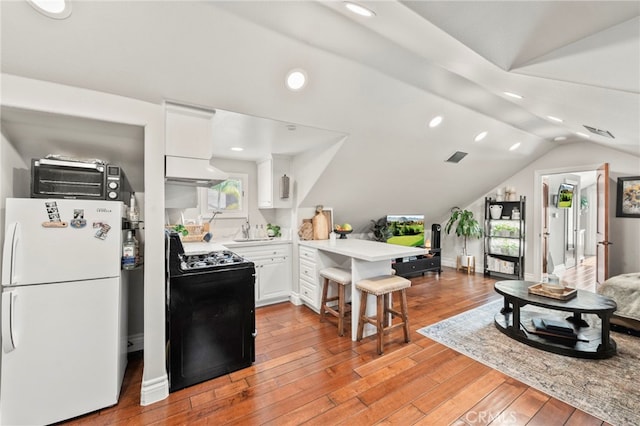 kitchen featuring white fridge, lofted ceiling, a breakfast bar area, black range with gas cooktop, and white cabinetry