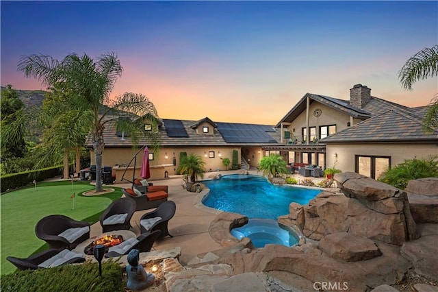 pool at dusk with a patio area and an in ground hot tub