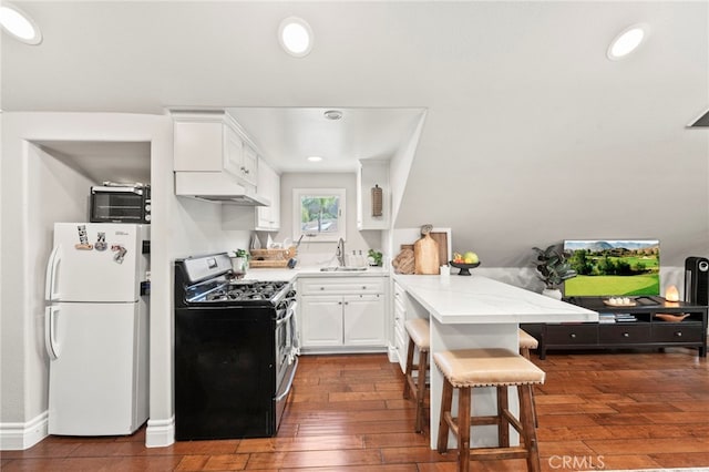 kitchen with sink, stainless steel range with gas cooktop, white cabinets, white fridge, and a kitchen bar