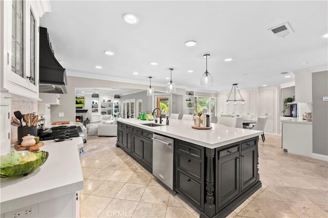 kitchen featuring stainless steel dishwasher, decorative light fixtures, a center island with sink, built in shelves, and sink