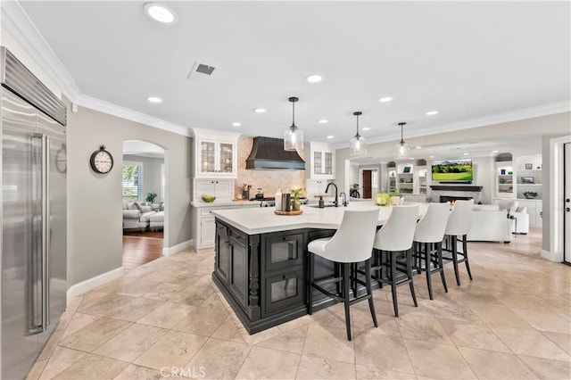 kitchen with premium range hood, hanging light fixtures, a spacious island, ornamental molding, and built in refrigerator