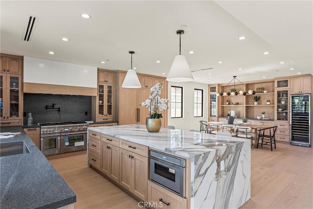 kitchen featuring stainless steel appliances, dark stone counters, a spacious island, decorative light fixtures, and light hardwood / wood-style floors