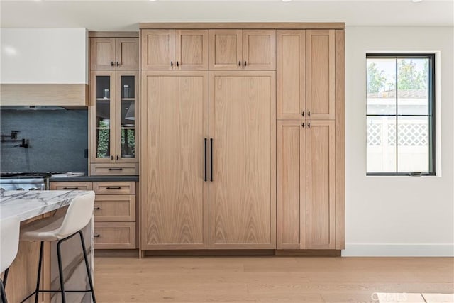 kitchen with a kitchen bar, decorative backsplash, light stone counters, and light wood-type flooring