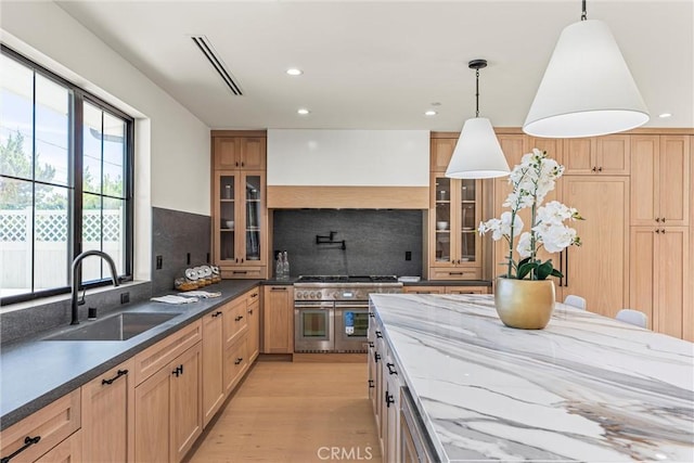 kitchen with double oven range, sink, tasteful backsplash, decorative light fixtures, and light hardwood / wood-style floors