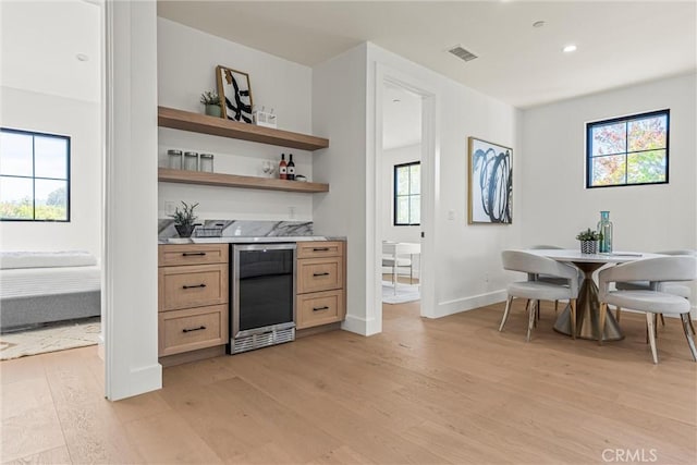 bar with a healthy amount of sunlight, beverage cooler, and light hardwood / wood-style floors