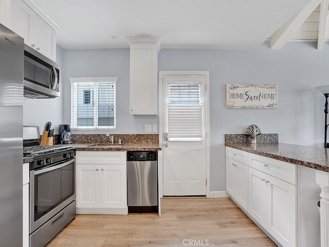 kitchen with light hardwood / wood-style flooring, sink, white cabinetry, dark stone counters, and stainless steel appliances