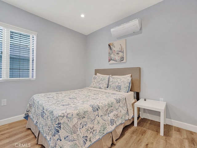 bedroom with light hardwood / wood-style floors and an AC wall unit