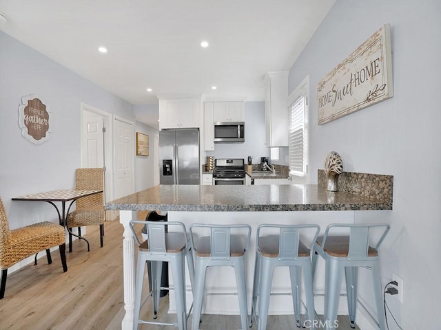 kitchen featuring light wood-type flooring, kitchen peninsula, a breakfast bar, appliances with stainless steel finishes, and white cabinets