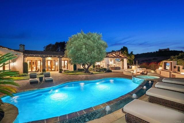 pool at dusk with a patio area, an in ground hot tub, and an outdoor fireplace