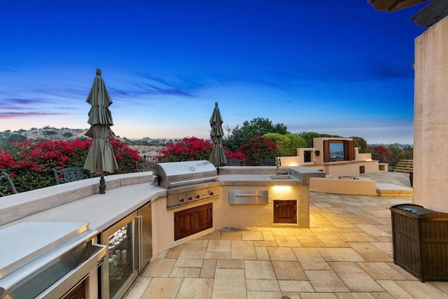 patio terrace at dusk with area for grilling, exterior kitchen, and sink