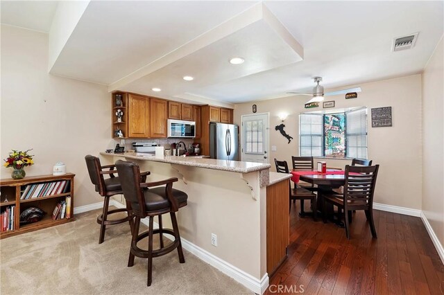 kitchen with sink, stainless steel fridge, kitchen peninsula, light stone counters, and a breakfast bar