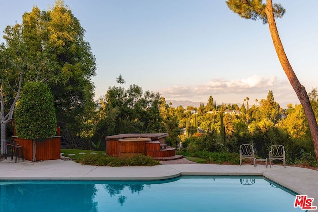 pool at dusk with a hot tub and a patio