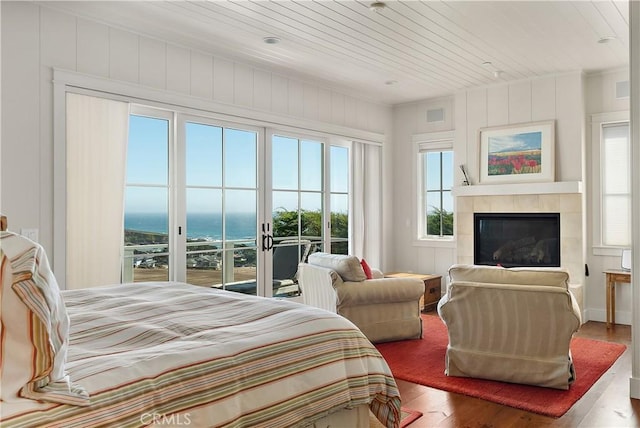 bedroom featuring access to exterior, wood ceiling, hardwood / wood-style flooring, a water view, and a fireplace