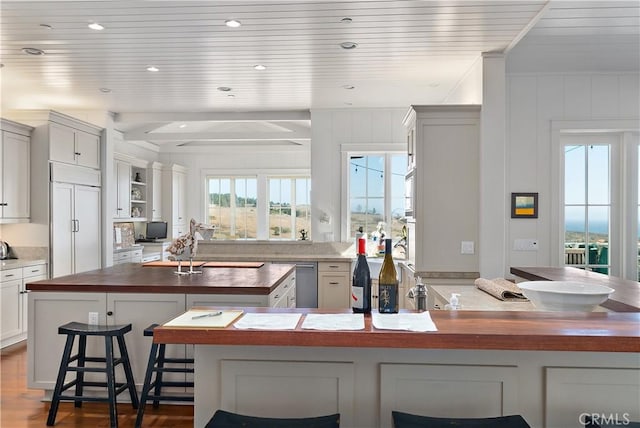 kitchen with hardwood / wood-style floors, white cabinets, paneled built in refrigerator, butcher block counters, and a breakfast bar area