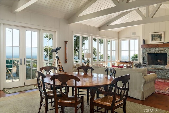 dining room with a stone fireplace, french doors, dark hardwood / wood-style floors, and vaulted ceiling with beams