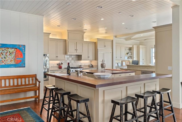 kitchen featuring dark wood-type flooring, wooden ceiling, a kitchen bar, a kitchen island with sink, and appliances with stainless steel finishes