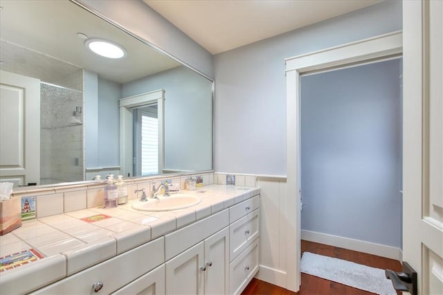 full bath with a tile shower, vanity, and wood finished floors