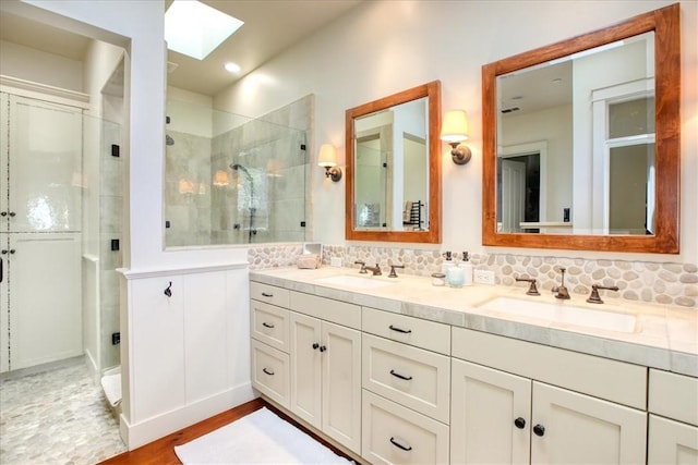 full bathroom featuring a skylight, tiled shower, double vanity, and a sink