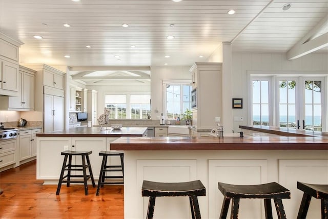 kitchen featuring built in appliances, butcher block counters, a kitchen bar, beamed ceiling, and light wood finished floors