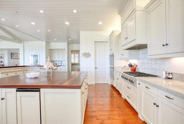 kitchen featuring gas cooktop, a large island, light wood finished floors, wooden counters, and decorative backsplash