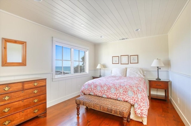 bedroom with visible vents, wood ceiling, crown molding, wood finished floors, and a wainscoted wall