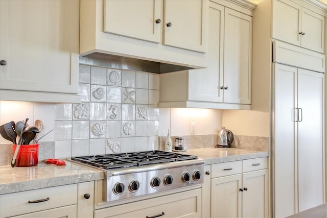 kitchen with paneled fridge, tasteful backsplash, stainless steel gas stovetop, light stone counters, and premium range hood