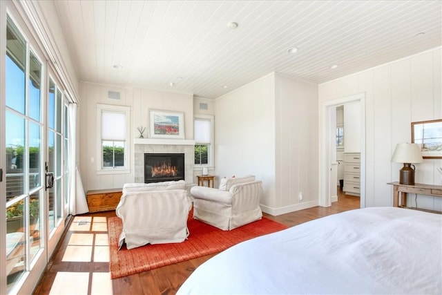bedroom with baseboards, wood ceiling, wood finished floors, access to exterior, and a glass covered fireplace