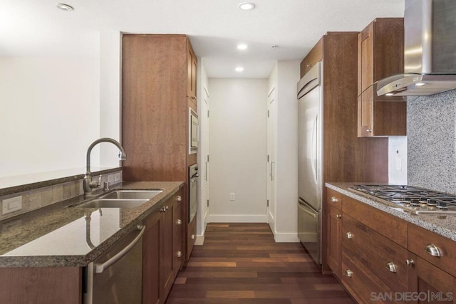 kitchen with sink, built in appliances, wall chimney exhaust hood, dark hardwood / wood-style floors, and decorative backsplash