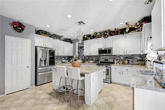 kitchen featuring a kitchen breakfast bar, light stone counters, white cabinets, a kitchen island, and stainless steel appliances