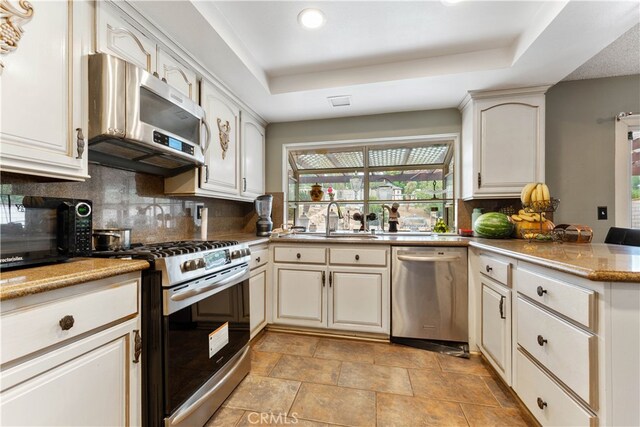 kitchen featuring appliances with stainless steel finishes, kitchen peninsula, a tray ceiling, and sink