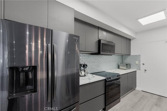 kitchen with stainless steel appliances, light stone counters, light hardwood / wood-style floors, gray cabinets, and decorative backsplash