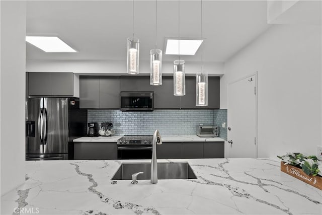 kitchen featuring a skylight, sink, stainless steel appliances, backsplash, and pendant lighting