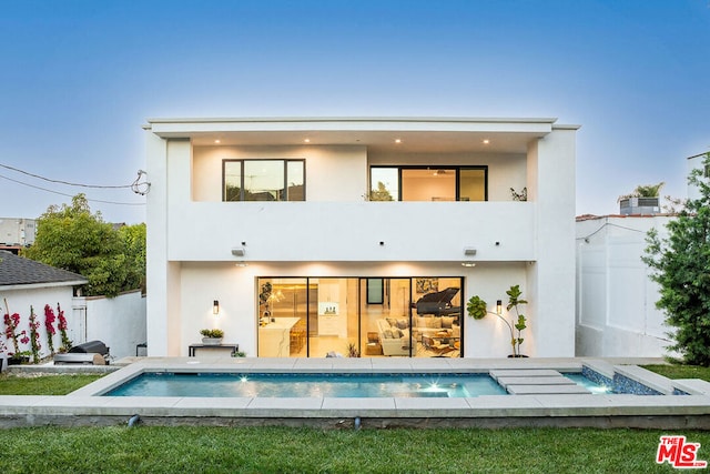 back house at dusk featuring a swimming pool with hot tub, pool water feature, and a balcony