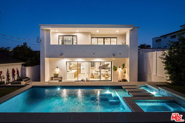 back house at night with a swimming pool with hot tub and a balcony