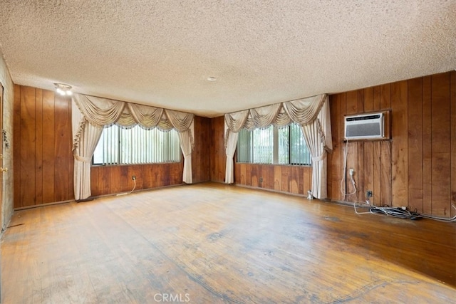 unfurnished room featuring hardwood / wood-style flooring, wood walls, a textured ceiling, and a wall mounted AC