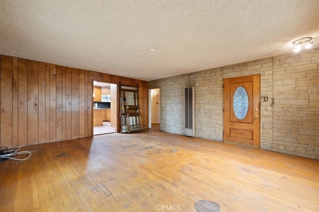 unfurnished living room featuring light wood-type flooring, wood walls, and a textured ceiling