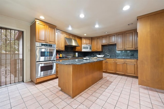 kitchen with dark stone counters, a kitchen island, backsplash, appliances with stainless steel finishes, and light tile patterned floors