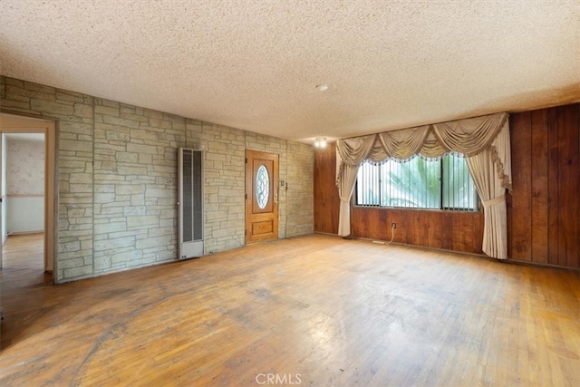 spare room featuring light hardwood / wood-style flooring, wooden walls, and a textured ceiling