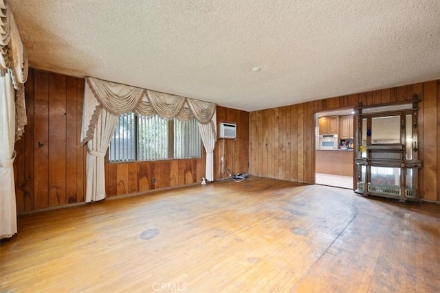 unfurnished living room featuring light hardwood / wood-style floors, wood walls, and a wall mounted AC