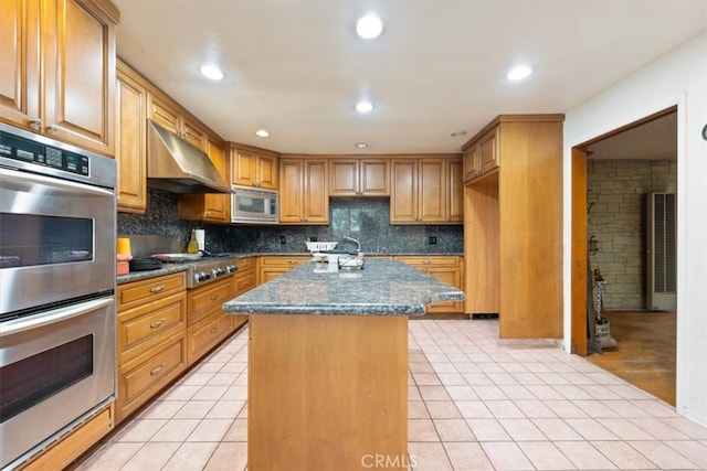 kitchen with light hardwood / wood-style floors, dark stone countertops, tasteful backsplash, a kitchen island, and stainless steel appliances